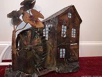 Full view of metal art grist mill sculpture showing the building, large wheel, and attached foliage.