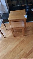 Set of two wooden nesting tables stacked, visible scratches on surfaces, light wood finish.