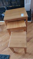 Three wood nesting tables viewed from above, stacked nested. Light wood with visible wear.