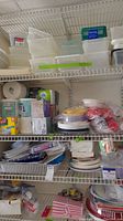 Shelving with stacked containers, rolls of paper towels, boxed kleenex, disposable plates stacked and wrapped, plastic cups and forks.