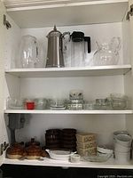 Three shelves of assorted kitchen items showing pitchers, bowls, ramekins, bean pots, and bakeware.