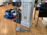 Metal rectangular pot rack with grid design laid on floor leaning against wall, chains and hooks placed at the base.