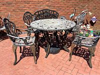 Wrought iron round table with four matching chairs in weathered condition on brick patio.