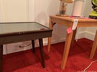 Side view of dark wooden shadow box table with glass top and part of adjacent light wood table.