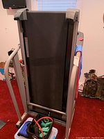 Folded treadmill with exercise mat and fitness accessories stored in front.
