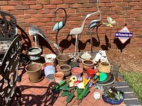 Photo of metal bird lawn art and assorted flower pots against brick wall.