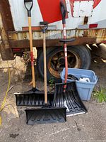 Photo showing three snow shovels arranged with handles upright and blades facing forward against a truck tire.