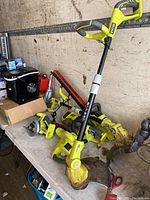 Wide view showing all six Ryobi tools including hedge trimmers, grass trimmers, circular saw, and charger on a table.