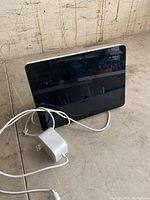 Front view of Amazon Echo Show screen powered off, with attached white power cord and adapter.