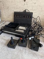 Full view of the ColecoVision console with AC adapter, two joystick controllers, and cables lying on a flat surface.