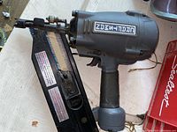 Gray and black Craftsman pneumatic nailer with coil nail magazine, showing tool details and nail attachments