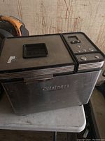 Front and top view of stainless steel Cuisinart bread maker showing control panel and lid window.