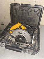 DeWalt yellow and black corded circular saw inside black carrying case on white surface, showing dust and signs of use.