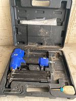Finishing nailer in black plastic case with hex keys and oil bottle