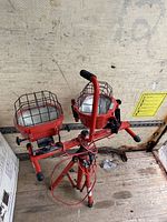 Pair of red Husky flood lights mounted on tripod with protective cage and handles, visible wiring and adjustable stand.