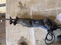Blue and black Mastercraft corded reciprocating saw with attached power cord on tiled floor.