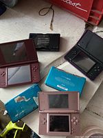 Five consoles open and closed on a white bench showing top and bottom shells and screens.