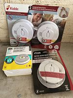 Photo showing three different new smoke detectors, including Kidde and BRK brands in packaging.