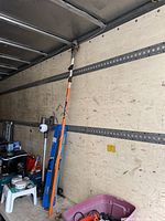Full view of the Fiskars telescoping branch clippers showing the long orange pole stored inside a vehicle with other tools.