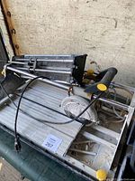 Overall view of wet tile saw showing handle, power cord, sliding aluminum tray, and water feed system.