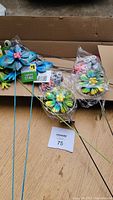 12 metal garden stakes with various colorful decorative designs including blue birds with pink flowers and green frogs, displayed in cardboard box.