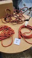 Photo showing three orange extension cords on a wooden table, one tangled, two coiled, with black electrical tape on some sections.