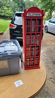 Photo of red telephone booth shaped CD holder filled with CDs, showing label and design.