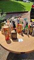Lot of assorted cleaning sprays and garden pesticides on outdoor wooden table.