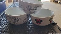 Three Disney ceramic bowls, two featuring Mickey Mouse sketches and one with Pluto line art on a grid background, and one with Minnie Mouse bow design.