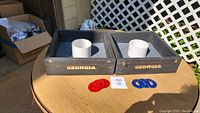 Two black wooden washer game boxes with white circular targets labeled 'Georgia' and red and blue washers on a round table outdoors.