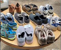 Photo showing various shoes on round table including sandals, casual and athletic shoes multiple colors and brands