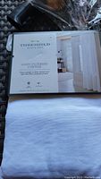 Photo of packaged Threshold branded white light-filtering curtain panel with rod pockets, showing dimensions and product details on label.