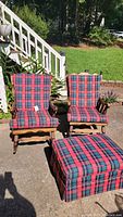 Two vintage wooden rocking chairs with red and black plaid cushions and a matching ottoman, outdoor setting on concrete patio.