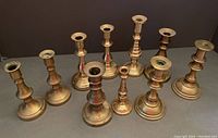 Top-down view of all 10 brass candlesticks arranged in two pairs and six single pieces shows size, shape, and finish variety