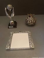 Overview photo of the three silver Judaica items: paper pad holder, hands holding Jerusalem globe, and Jewish Jerusalem globe sculpture with dove.