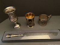 Photo showing all 4 items: Sterling-like chalice, gold-tone cup, silver plate cup holder, and serrated Shabbat knife in box.