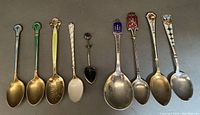 Full view of all 9 spoons showing various designs and enamel colors, some with twisted handles; green spoon shows enamel damage.