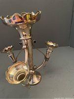 Front-close view of the silver plated epergne showing the main tall central trumpet-shaped vase with scalloped edge and three attached ornate branches ending in smaller trumpet-shaped vases.