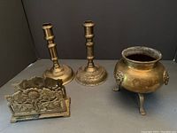Wide shot showing all three brass items together on a flat surface against a dark background.