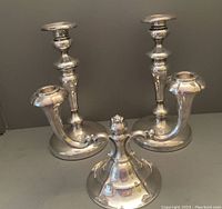 Two silver plate candlesticks and one two-branch silver plate candelabra arranged together showing full shape and design.