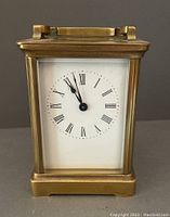 Front view of brass carriage clock with white dial and black Roman numerals and hands