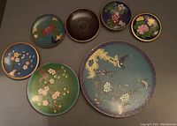 Overview of all 7 cloisonné plates grouped together showing size variation and designs