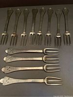 Close up of 7 pewter forks showing the trefid pattern on the handles, aged with slight patina.