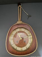 Front view of vintage Garant Schwebe Anker wall clock showing wooden body, dial with Roman numerals, and attached key with knotted cord.