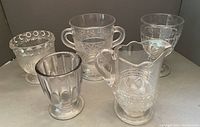 Full set of four different pressed glass spooners and one small pitcher shown together.