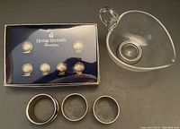 Set of six silver plate shell motif place-card holders in a box and three engraved napkin rings laid out with glass sauce boat.