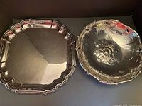 Both silver plated items side by side showing bowl with ornate embossed floral design and square tray with scalloped edges