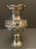 Front view of silver-plated vase showing detailed repoussé floral and scroll work on its bulbous body and scalloped rim.