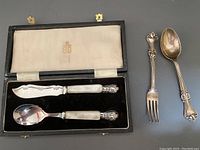 Boxed set containing silver plate and mother of pearl baby knife and spoon with branding on white satin interior lining.