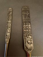 Close-up view of handles of pewter fork and ladle with Viking relief scenes